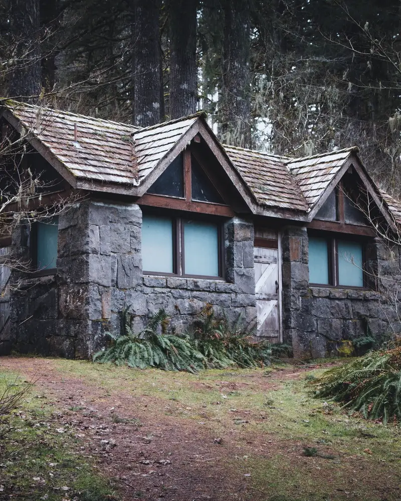 A stone cottage with a shingled roof among tall trees