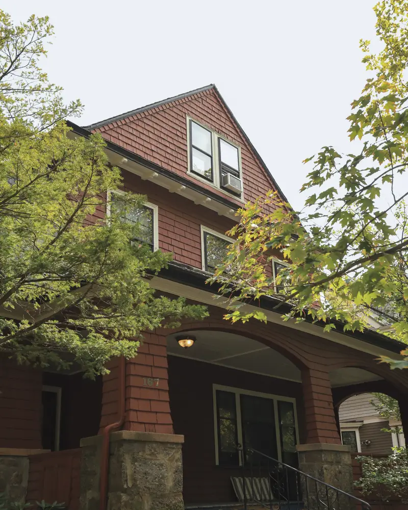 A brick craftsman house with a deep porch under trees