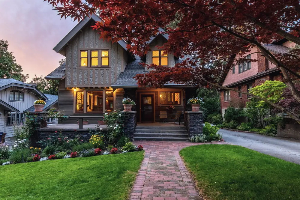 A craftsman house at dusk with lit windows and a brick front walk