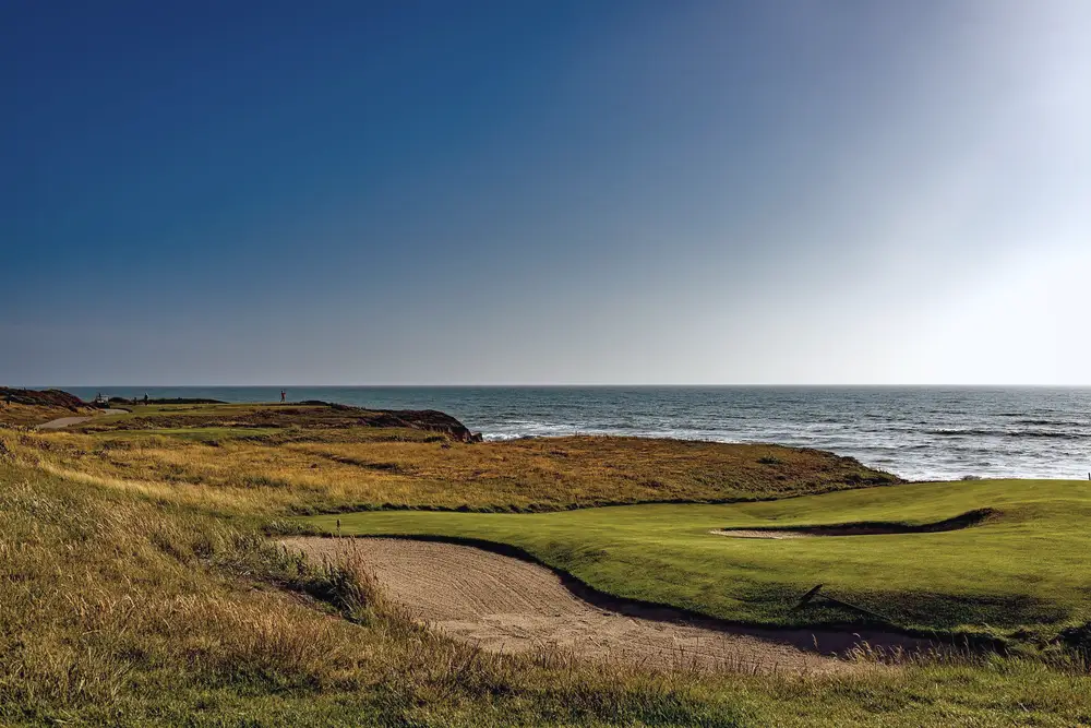 A links-style golf course running down to the water under a clear sky