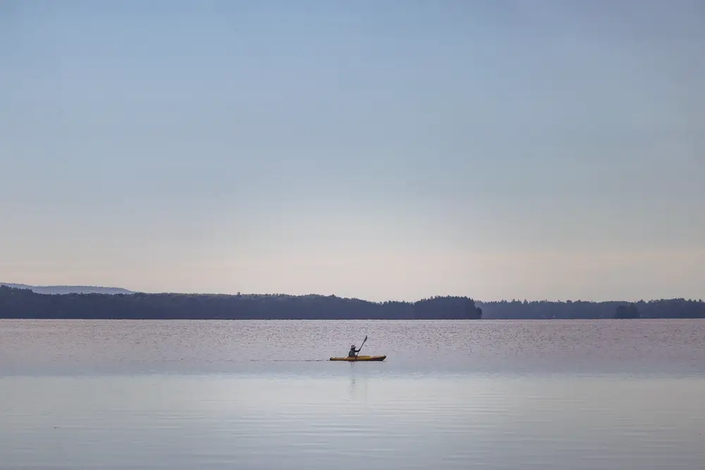 A lone kayaker on still water in soft morning light